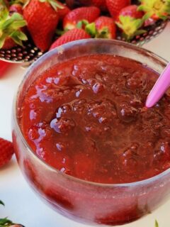 Strawberry jam in a bowl with raw strawberries around it image