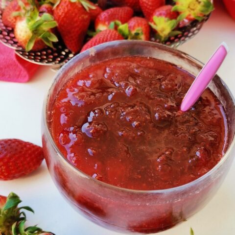 Strawberry jam in a bowl with raw strawberries around it image