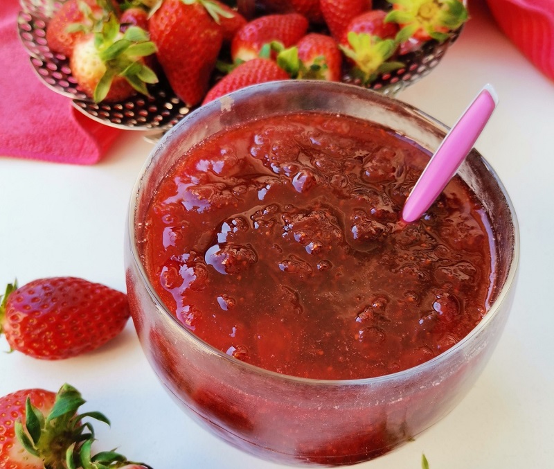 Strawberry jam in a bowl with raw strawberries around it image
