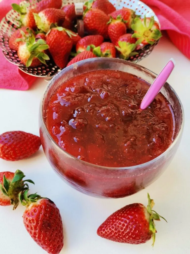 Strawberry jam in a bowl with raw strawberries in the background and in front of it image