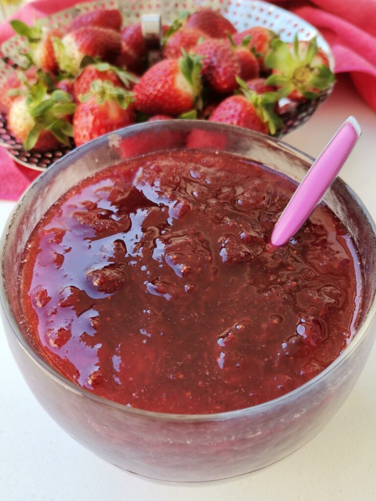 Strawberry jam in a bowl with raw strawberries in the background image