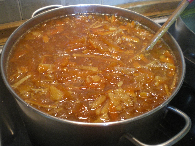 A pot full of citrus marmalade with a wooden spoon image